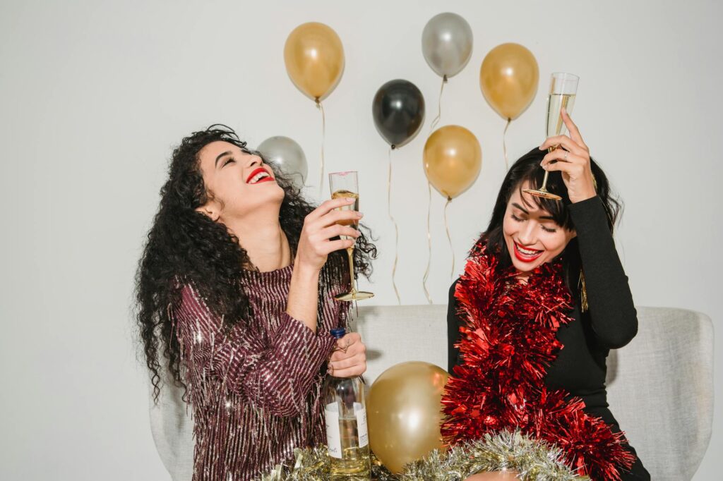 Happy smiling friends with bright red lips and glasses of crystal champagne and red sparkling tinsel celebrating New Year